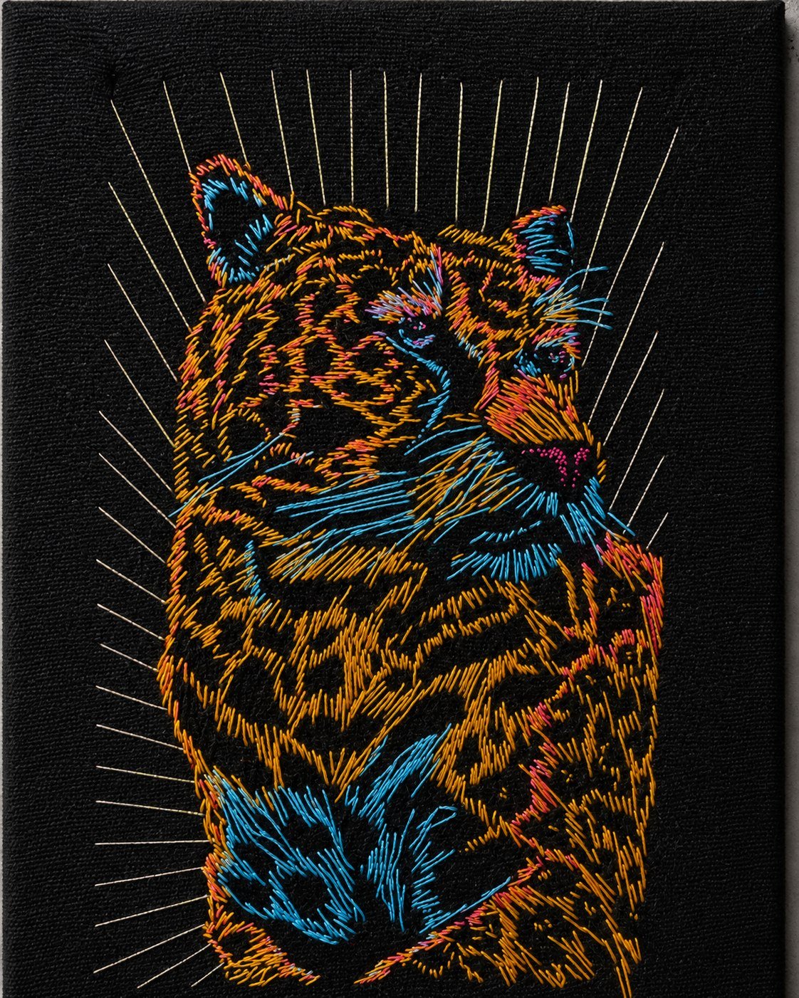 Detalle macro de un bordado de tigre, con hilos de color naranja y azul sobre fondo negro.